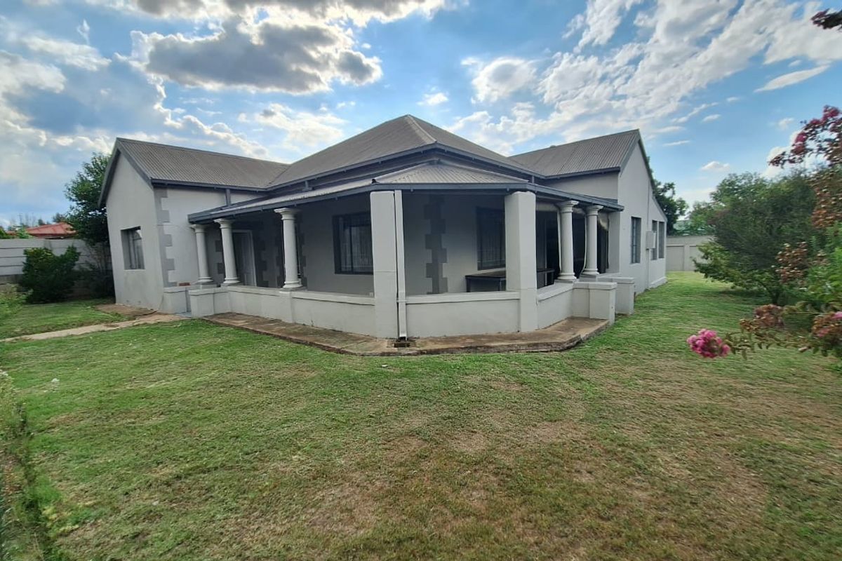 Rear view of the house featuring a wrap-around covered veranda with concrete columns, set within a spacious garden with a surrounding boundary wall.