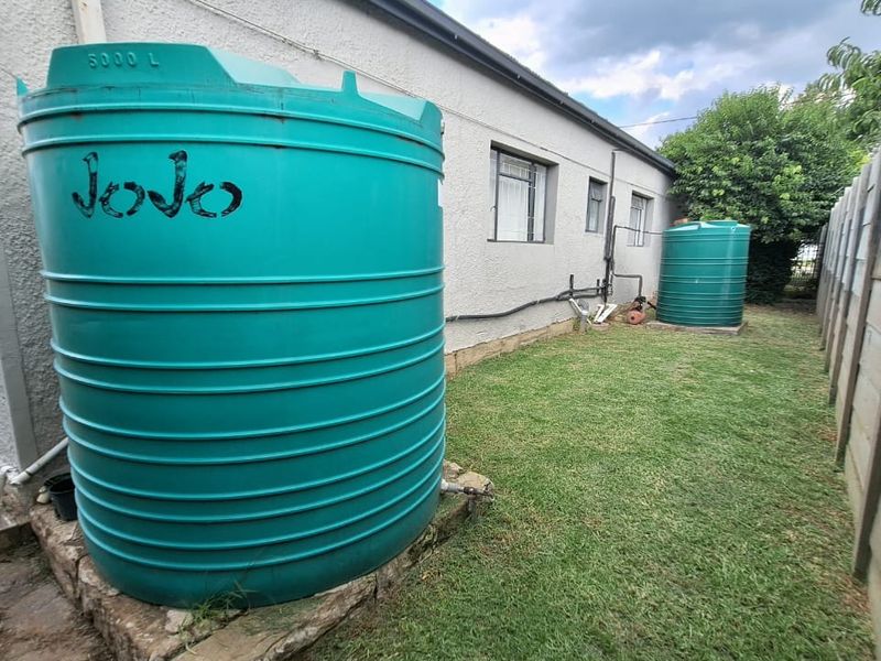 Rear exterior view of the property featuring two large water storage tanks, a grassed yard, and a precast concrete boundary wall.