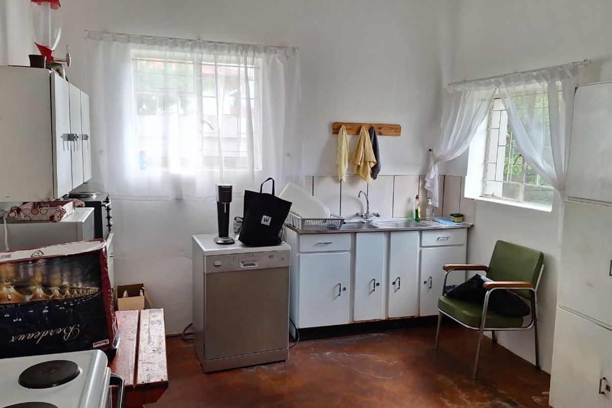 A dated kitchen featuring original cabinetry, a stainless steel sink, tiled splashbacks, and security bars on the windows.