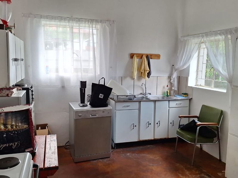 A dated kitchen featuring original cabinetry, a stainless steel sink, tiled splashbacks, and security bars on the windows.