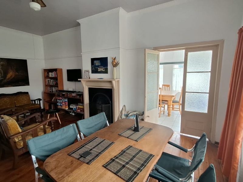 Open plan living and dining area featuring original timber flooring, a classic fireplace with mantelpiece, and french doors leading to an adjoining space.