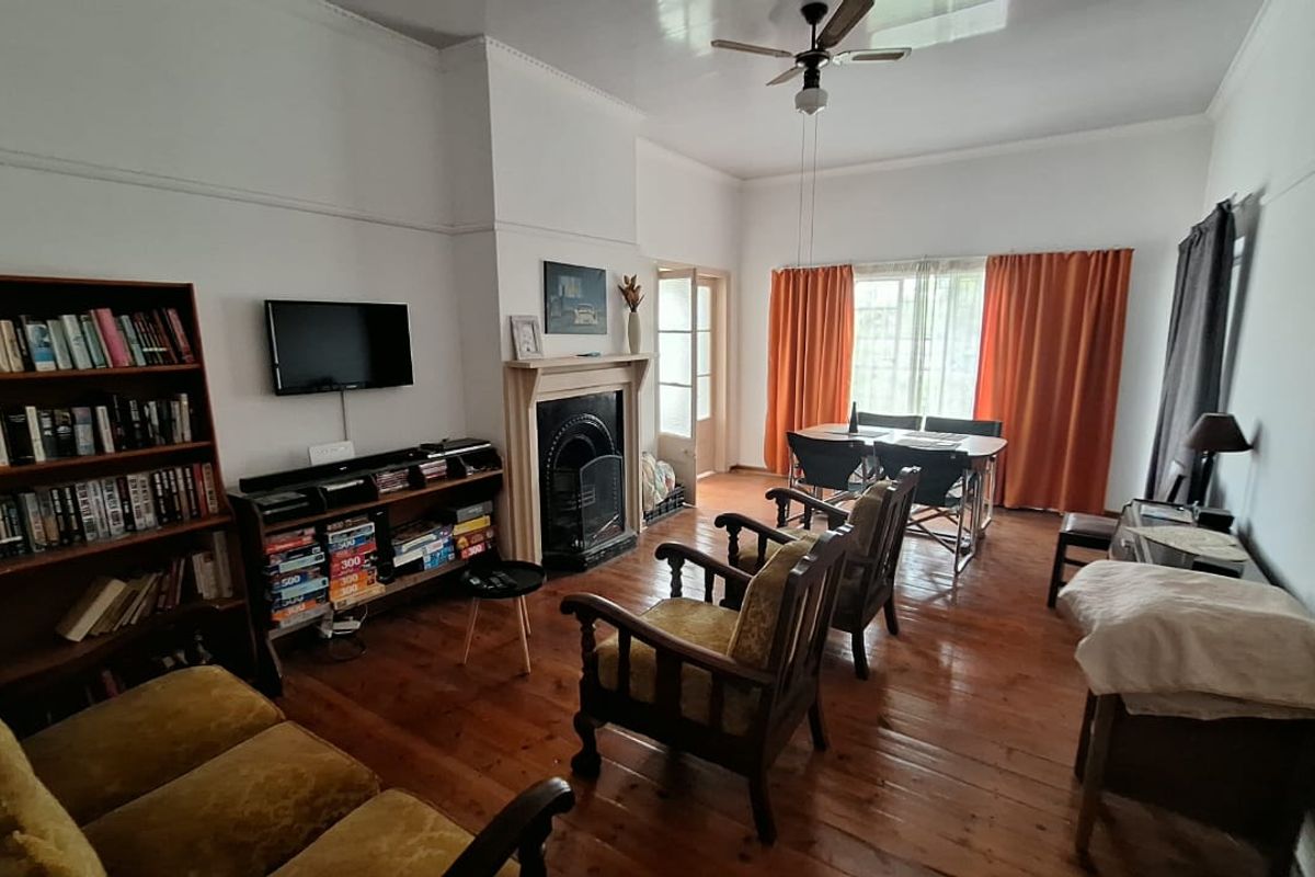 A living room featuring original hardwood flooring, a traditional fireplace, and a ceiling fan, offering a classic character feel.