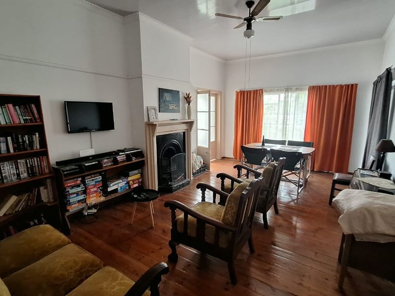 A living room featuring original hardwood flooring, a traditional fireplace, and a ceiling fan, offering a classic character feel.