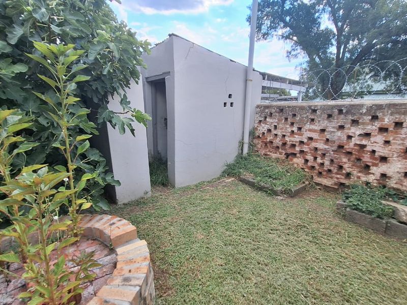 Rear garden area featuring a brick boundary wall with razor wire, a small utility outbuilding, and a circular brick planter.
