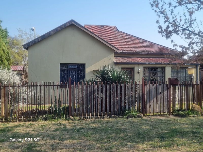Front view of a single-story house featuring a corrugated metal roof, security bars on windows, and a metal perimeter fence.