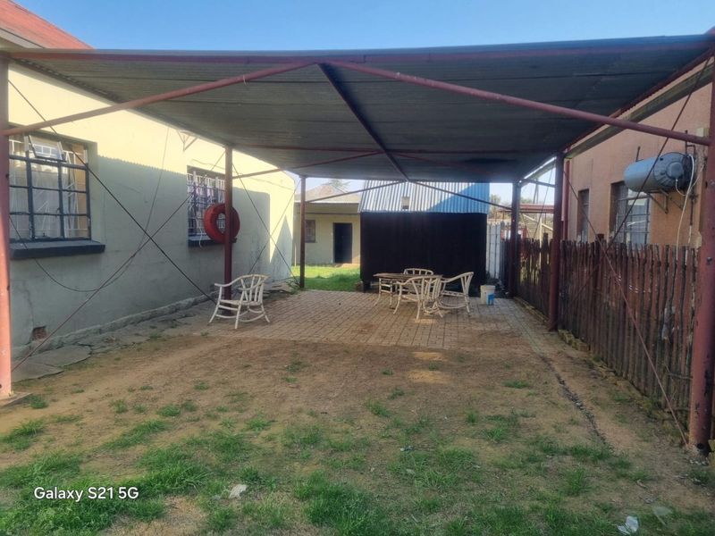 A covered outdoor patio area featuring a metal frame structure and paved flooring, situated between two residential building sections.