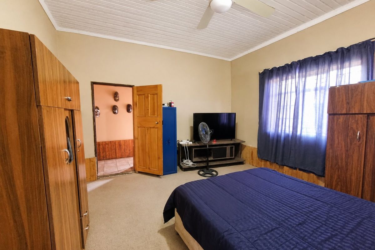 A bedroom featuring timber wall paneling, a ceiling fan, and carpeted flooring, offering a functional space with traditional finishes.