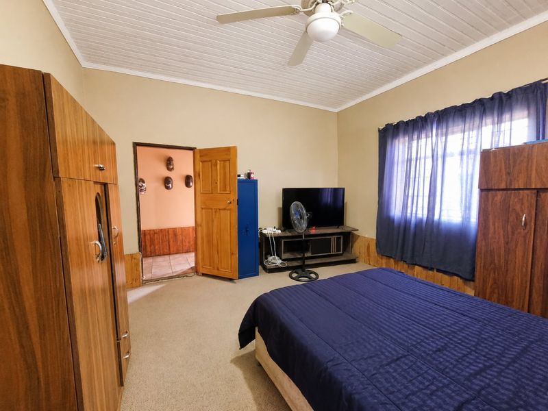 A bedroom featuring timber wall paneling, a ceiling fan, and carpeted flooring, offering a functional space with traditional finishes.