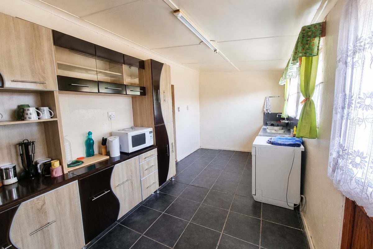 A functional kitchen featuring fitted cabinetry, dark tiled flooring, and a stainless steel sink, offering a practical layout with potential for modern updates.