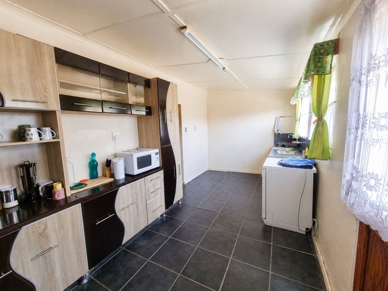 A functional kitchen featuring fitted cabinetry, dark tiled flooring, and a stainless steel sink, offering a practical layout with potential for modern updates.