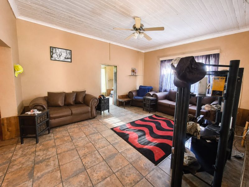 A living room featuring tiled flooring, a timber plank ceiling, and a central ceiling fan, offering a functional and dated living space.