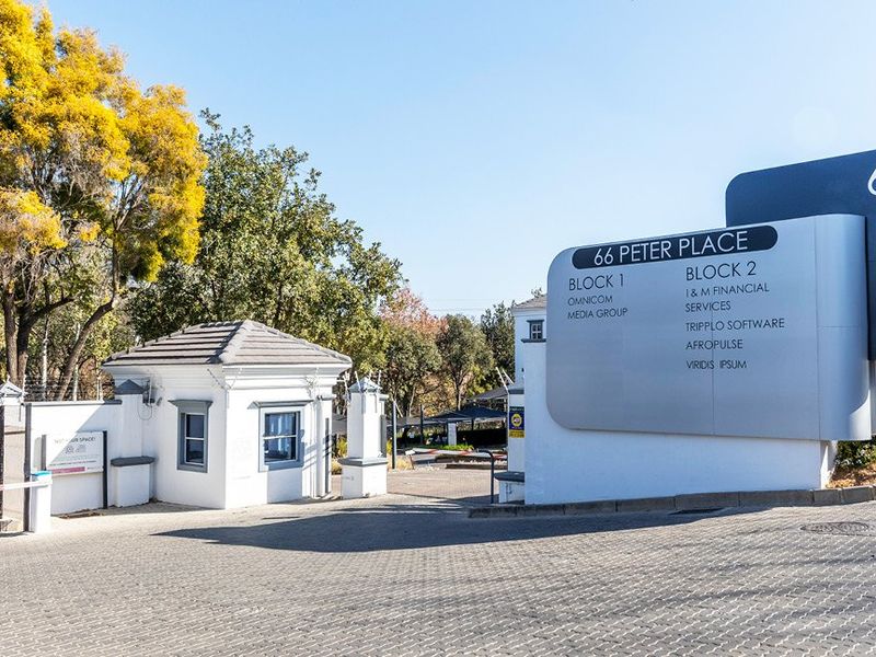 Front entrance of a commercial office park featuring a security guard house, paved driveway, and prominent signage for multiple business tenants.