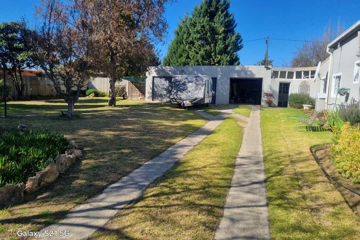 Rear garden view featuring a spacious lawn, concrete driveway, and a double garage structure.