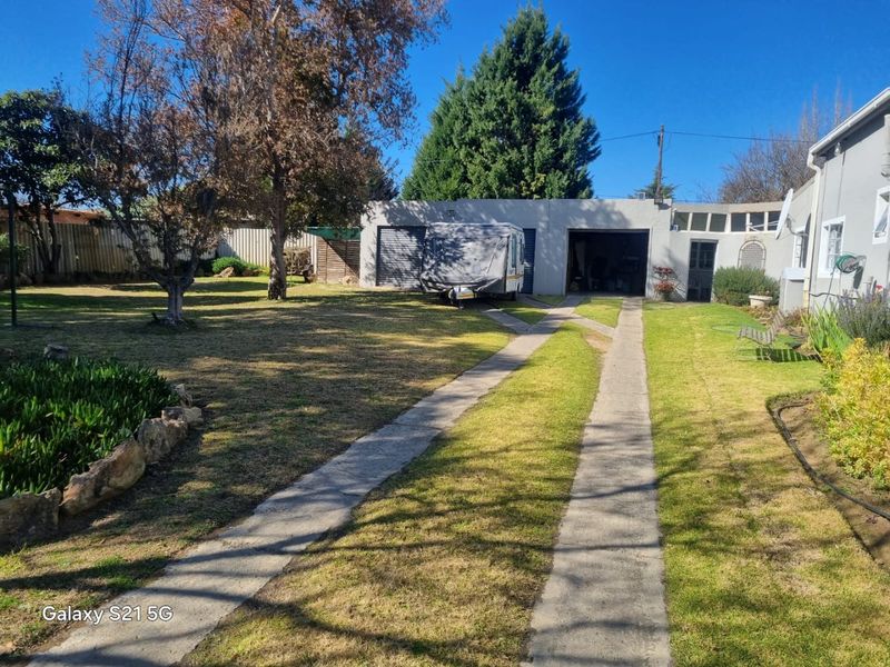 Rear garden view featuring a spacious lawn, concrete driveway, and a double garage structure.