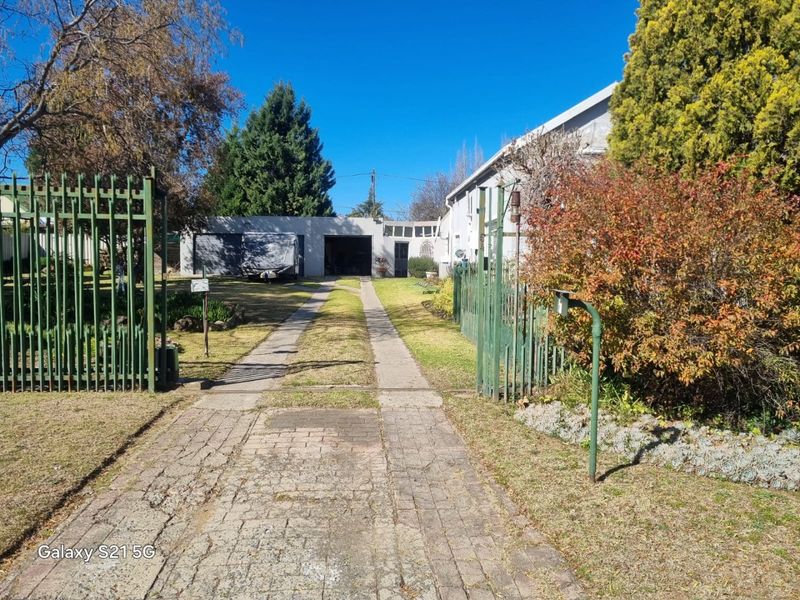 Front view of the property featuring a gated entrance, paved driveway leading to a garage, and established garden area.