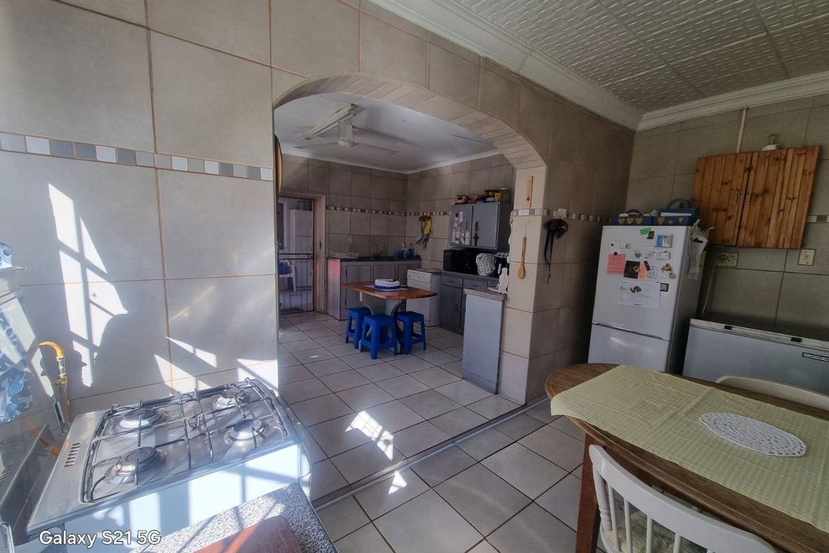 A functional kitchen featuring tiled walls and flooring, an arched entryway, and a gas hob, offering a dated layout ready for modernization.