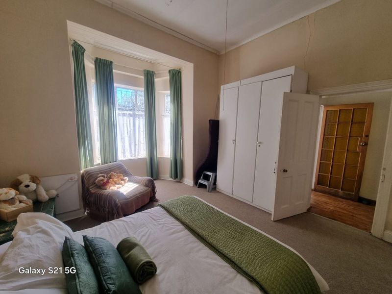A bedroom featuring a bay window, built-in wardrobe, and carpet flooring. The room shows signs of wear including visible wall cracks.