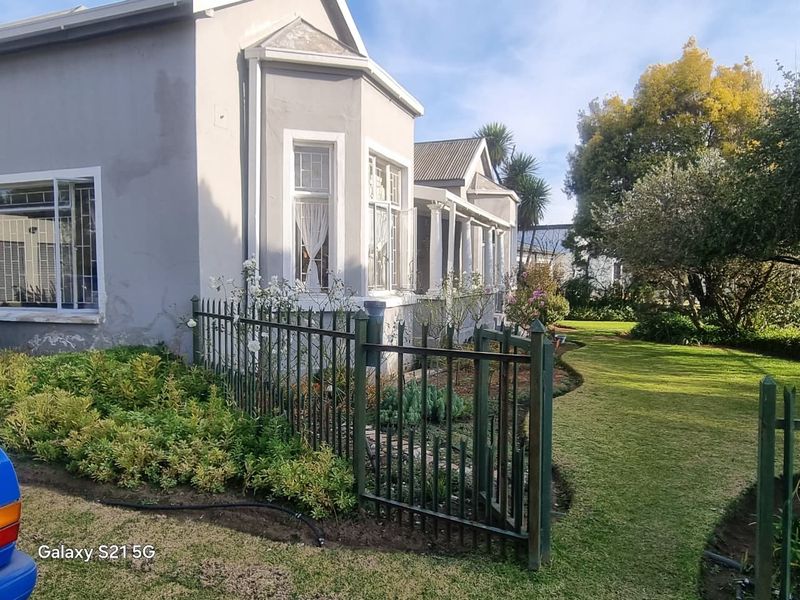 Front view of a house featuring a metal security fence, landscaped garden, and a covered veranda with columns.
