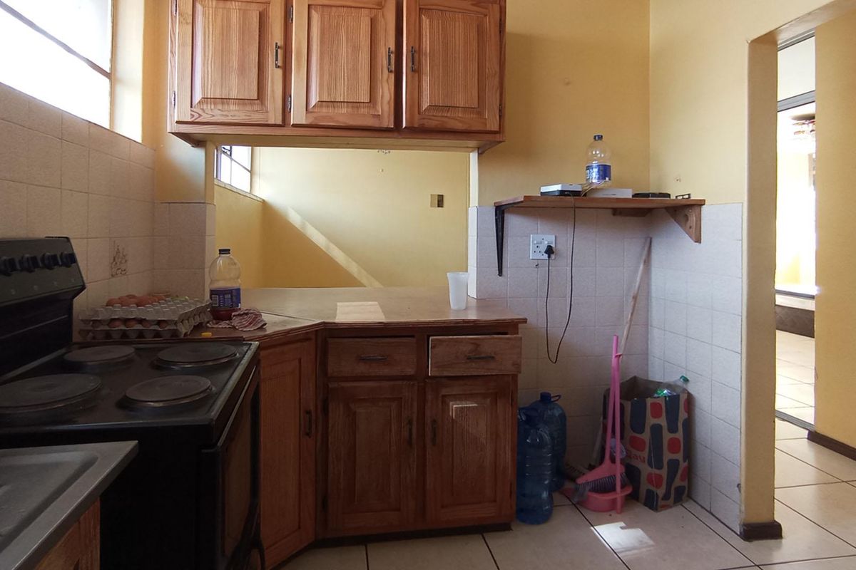 A dated kitchen featuring wooden cabinetry, tiled backsplash, and tiled flooring, offering a functional layout with potential for modern cosmetic updates.