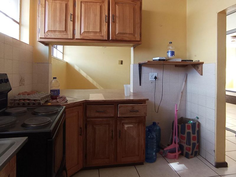 A dated kitchen featuring wooden cabinetry, tiled backsplash, and tiled flooring, offering a functional layout with potential for modern cosmetic updates.
