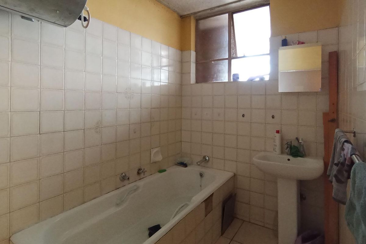 A dated bathroom featuring a standard bathtub, pedestal basin, and tiled walls. The space requires modernization and cosmetic updates to improve its condition.