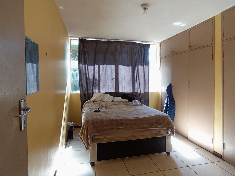 A bedroom featuring tiled flooring and extensive built-in cupboard storage, offering a functional layout in need of cosmetic updates.