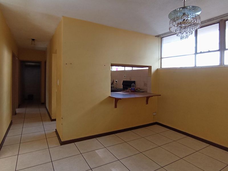 Open plan living area featuring ceramic floor tiles, a pass-through window to the kitchen, and a breakfast bar counter.