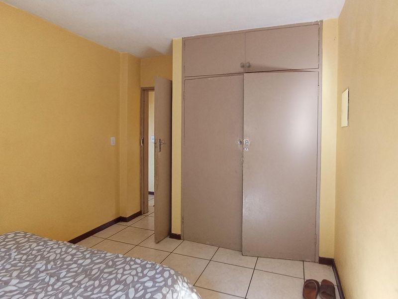 A bedroom featuring tiled flooring and built-in cupboards with overhead storage, offering a functional space with potential for cosmetic updates.