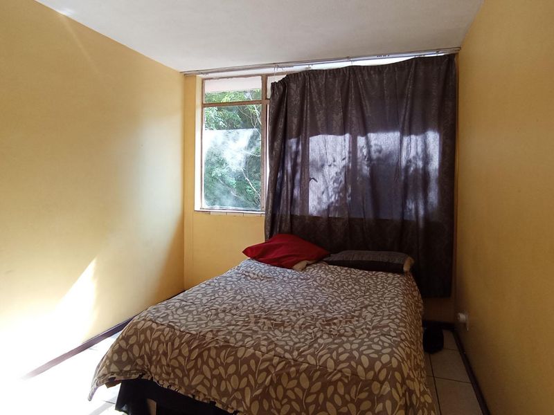 A bedroom featuring tiled flooring and a window with a curtain track, requiring cosmetic updates to the wall finishes.