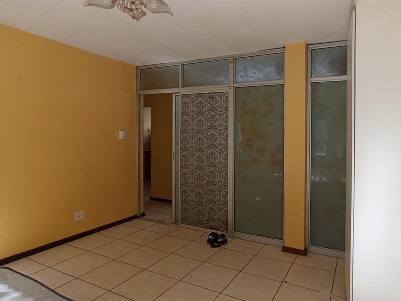 A bedroom featuring tiled flooring and an aluminium-framed glass partition wall, offering a blank canvas for renovation and modernization.