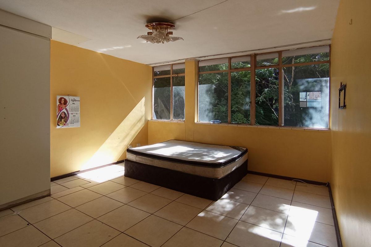 A spacious bedroom featuring tiled flooring, built-in wardrobes, and large windows that provide ample natural light.