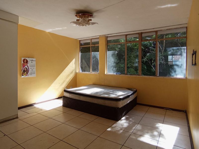 A spacious bedroom featuring tiled flooring, built-in wardrobes, and large windows that provide ample natural light.