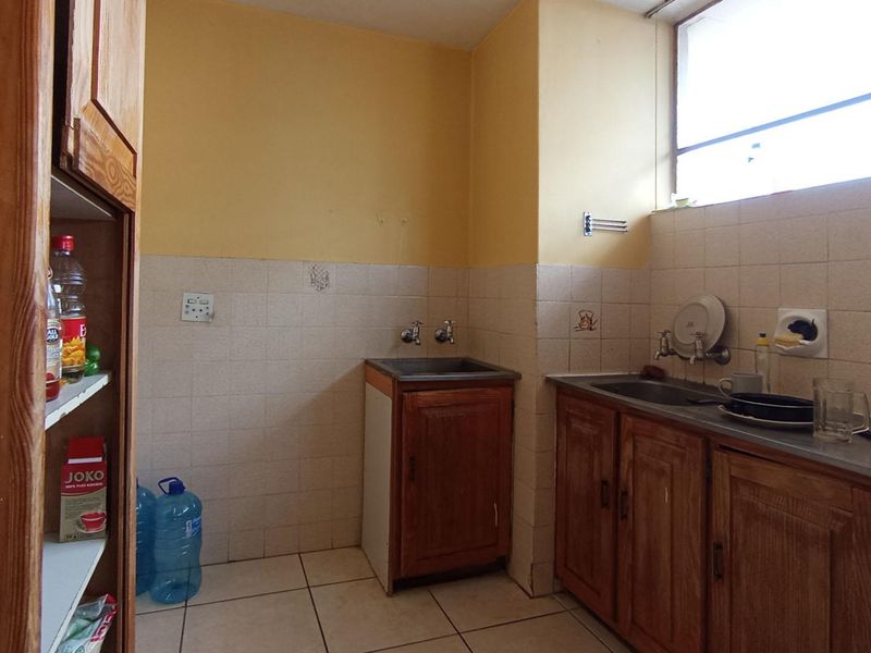 A functional kitchen area featuring built-in wooden cabinetry, stainless steel sinks, tiled splashbacks, and tiled flooring, offering potential for modernization.