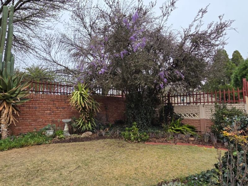 A private garden area featuring a well-established lawn, mature trees, and a secure perimeter defined by brick and precast concrete boundary walls.