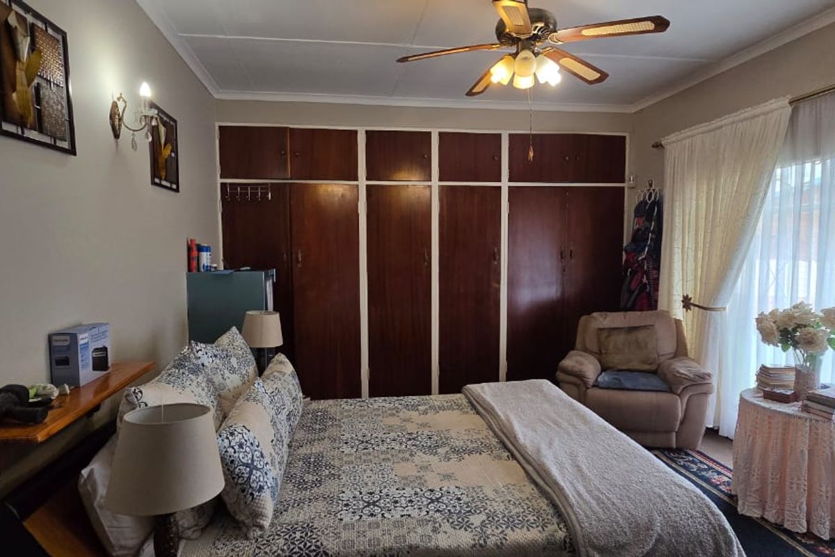 A bedroom featuring extensive built-in wooden cupboards, a ceiling fan, and a large sliding glass door providing natural light and access to the exterior.