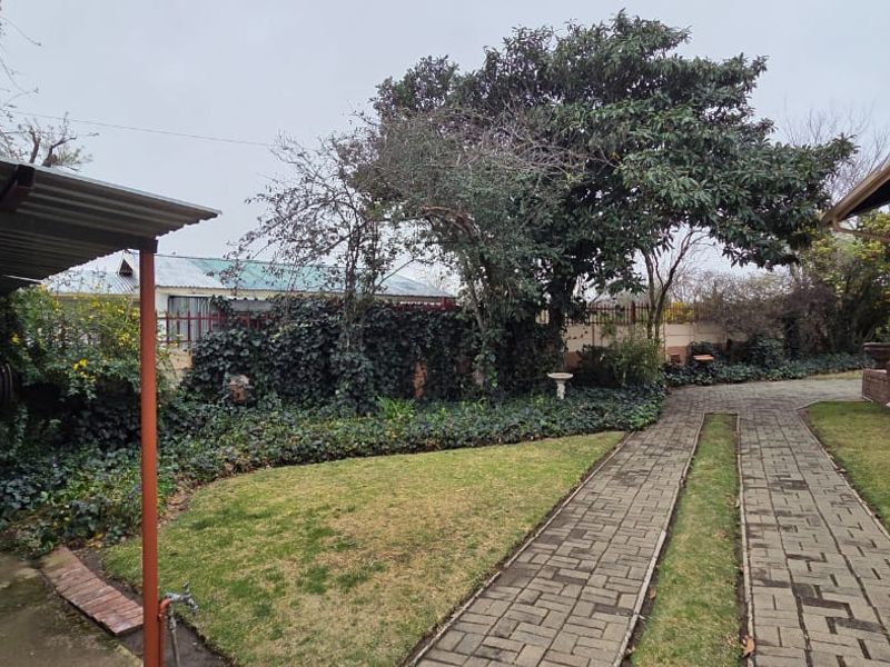 Front exterior view featuring a paved driveway, covered carport, and established garden area with security bars on the windows.