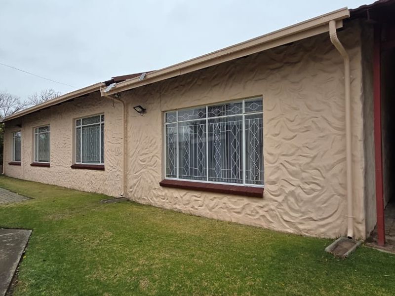 Rear exterior view of the house featuring textured stucco walls, security-barred windows, a paved driveway, and a covered carport area.