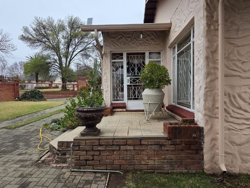 Front entrance view featuring a tiled porch, security gate, and textured exterior walls with brick detailing and paved driveway.