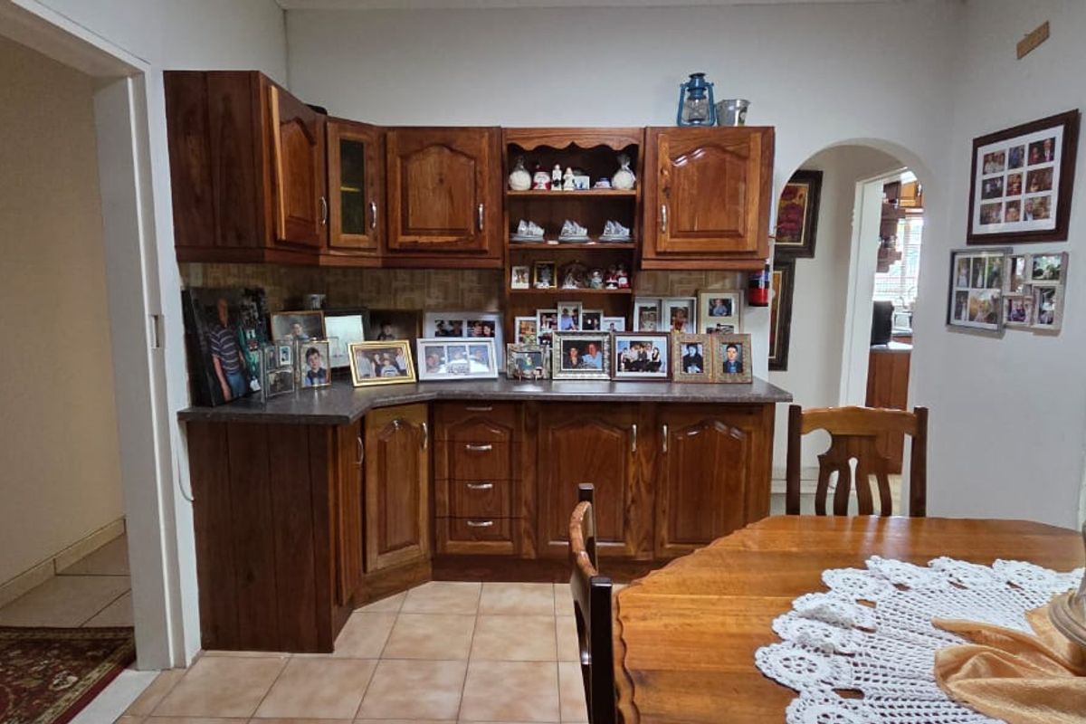 A kitchen area featuring traditional wooden cabinetry, laminate countertops, and tiled flooring, connected to adjacent living spaces via an archway.