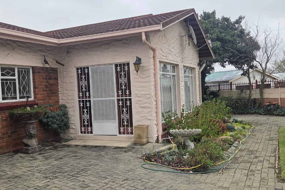 Rear exterior view of the house featuring a paved courtyard, brick and textured plaster facade, and secure entrance gate.
