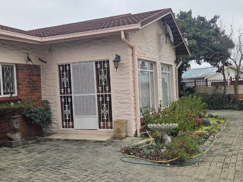 Rear exterior view of the house featuring a paved courtyard, brick and textured plaster facade, and secure entrance gate.