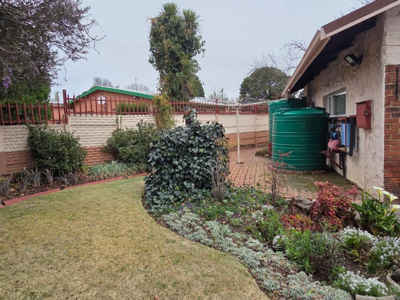 Rear garden area featuring a brick paved patio, water storage tanks, and a precast concrete boundary wall adjacent to the garage.