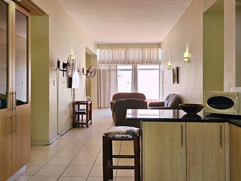 Open-plan living area featuring a functional kitchen with built-in cabinetry, granite countertops, and tiled flooring, leading to a bright lounge space.