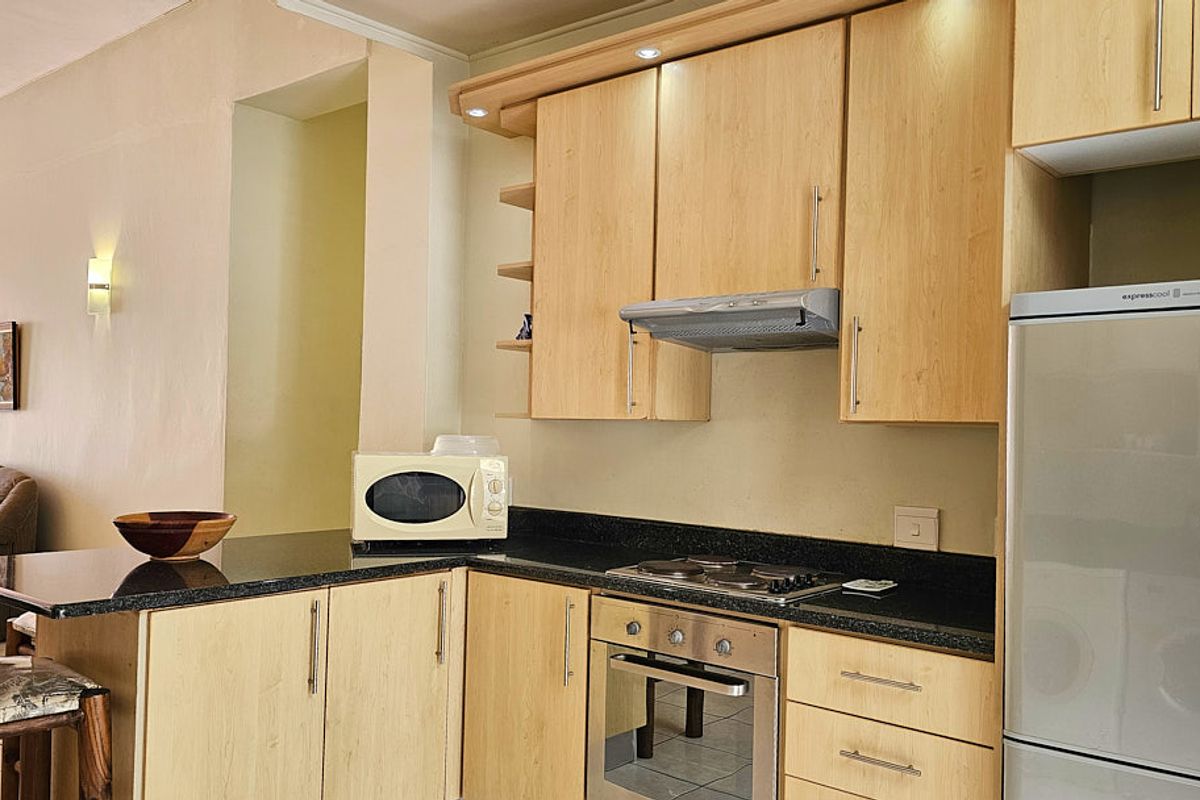 A functional kitchen featuring light wood cabinetry, granite countertops, and integrated appliances including an oven, hob, and extractor fan.