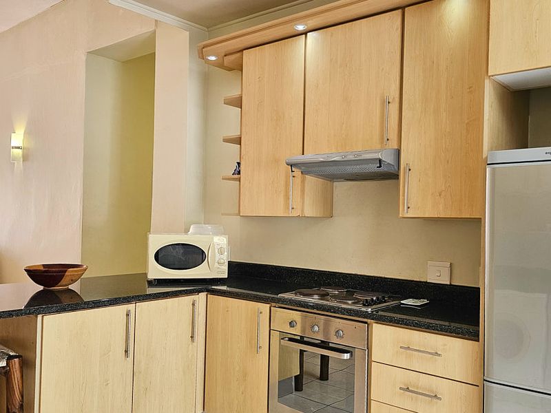 A functional kitchen featuring light wood cabinetry, granite countertops, and integrated appliances including an oven, hob, and extractor fan.
