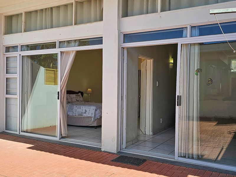 A paved patio area featuring large sliding glass doors that provide access to the interior living spaces and bedroom.