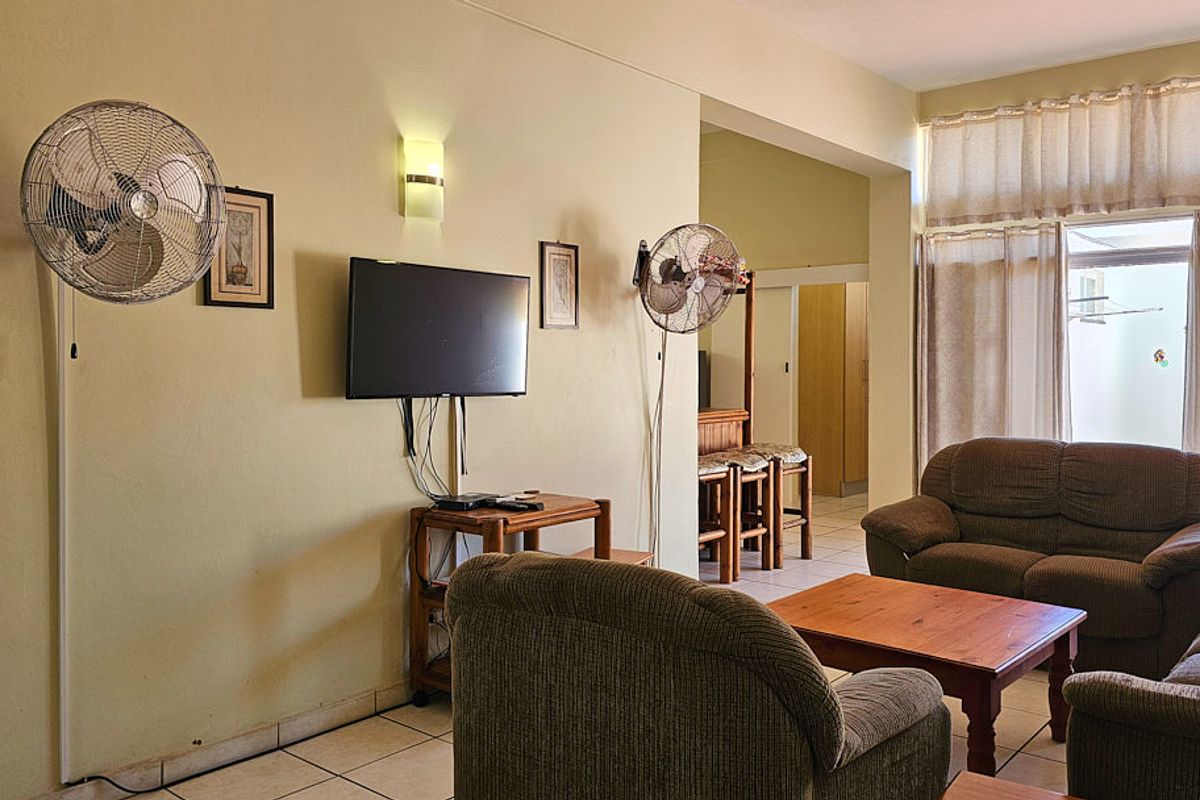 A living room area featuring tiled floors, wall-mounted fans, and a sliding glass door providing access to the exterior.