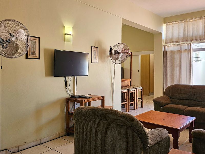 A living room area featuring tiled floors, wall-mounted fans, and a sliding glass door providing access to the exterior.