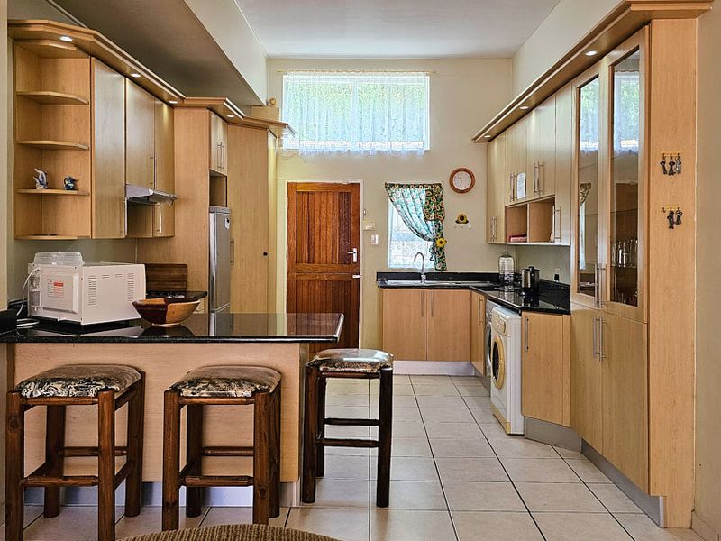 A functional kitchen featuring light wood cabinetry, granite countertops, integrated appliances, and tiled flooring with a breakfast bar area.
