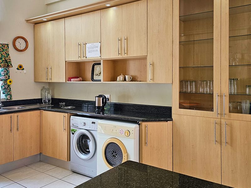 A functional kitchen featuring light wood cabinetry, dark granite countertops, and integrated laundry appliances, providing efficient storage and workspace.